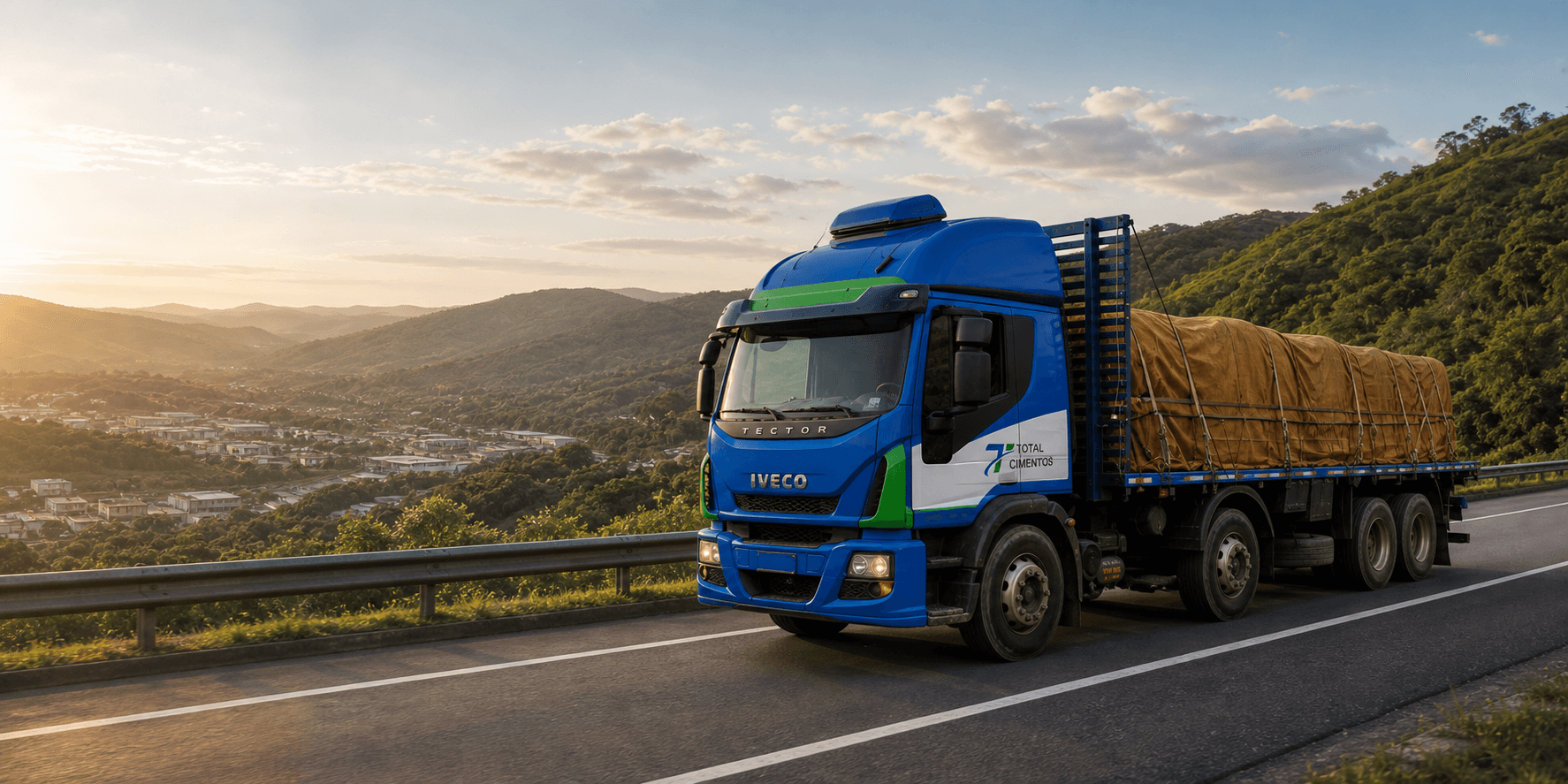 Caminhão azul e verde da Total Cimentos transportando carga coberta por lona em uma rodovia entre as montanhas de Minas Gerais